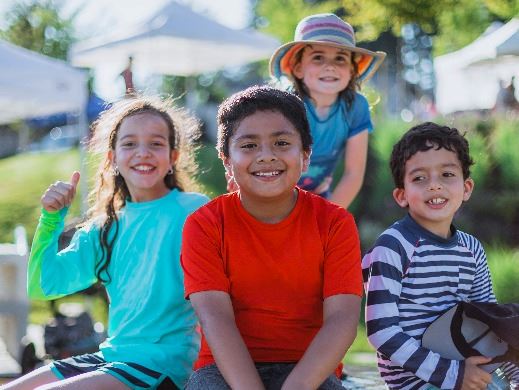  Four children in summer clothes sitting together outside and smiling at the camera.