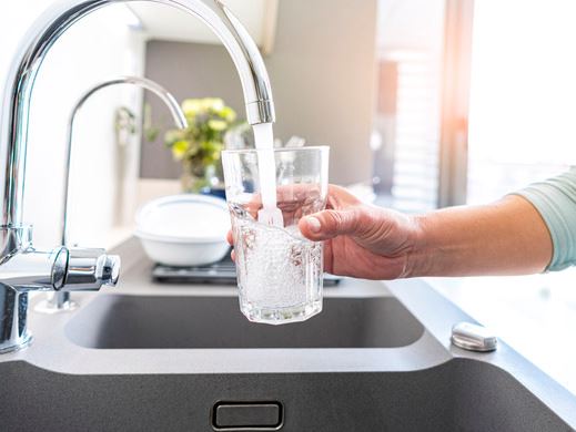 Kitchen faucet running clear water into a glass