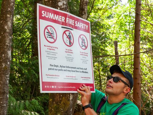 Parks staff member installing summer fire safety sign on tree in a Coquitlam park