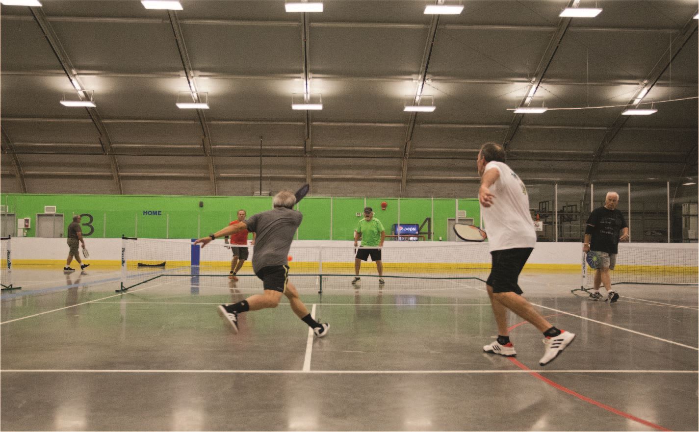 A group of adults play pickleball at an indoor court